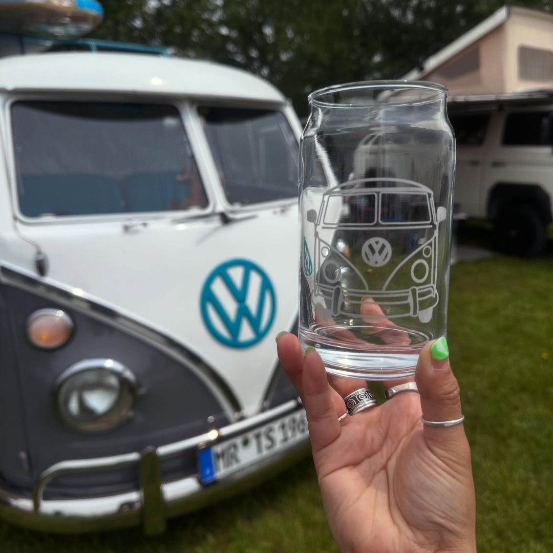 Hand holding a glass with a VW bus etching in front of a classic VW camper van.