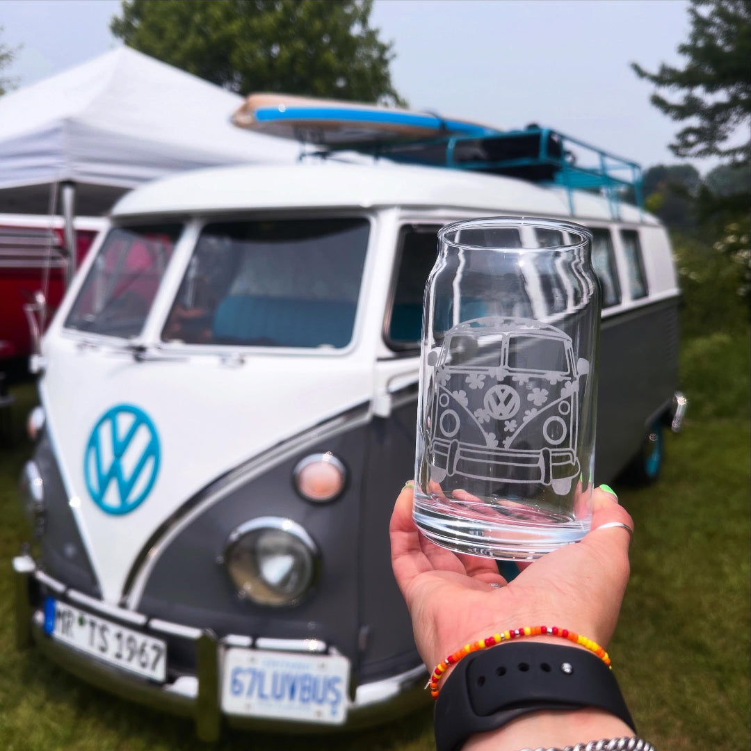 Hand holding a glass with a Volkswagen design in front of a vintage van.
