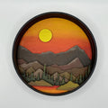 A Paint By Layers Craft Kit featuring a circular shadow box with a pre-designed landscape scene. The scene depicts a mountain range under a starry night sky, with a river flowing through a valley. The kit includes layers of wood, paint, and instructions. The title of the kit is "Rocky Mountain Shadow Box."