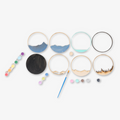 A Paint By Layers Craft Kit featuring a circular shadow box with a pre-designed landscape scene. The scene depicts a mountain range under a starry night sky, with a river flowing through a valley. The kit includes layers of wood, paint, and instructions. The title of the kit is "Rocky Mountain Shadow Box."