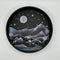 A Paint By Layers Craft Kit featuring a circular shadow box with a pre-designed landscape scene. The scene depicts a mountain range under a starry night sky, with a river flowing through a valley. The kit includes layers of wood, paint, and instructions. The title of the kit is 