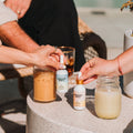 Two people preparing drinks with bottles labeled 'Bourbon Soda' on a table outdoors.