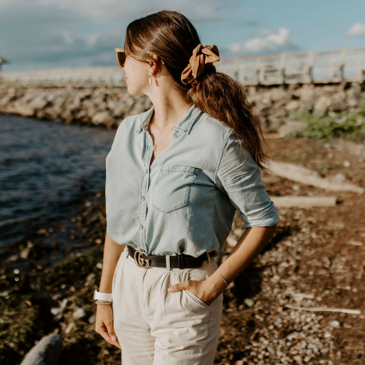 A rust-colored fabric scrunchie with a gathered, ruffled appearance. It has a small white tag with the word 
