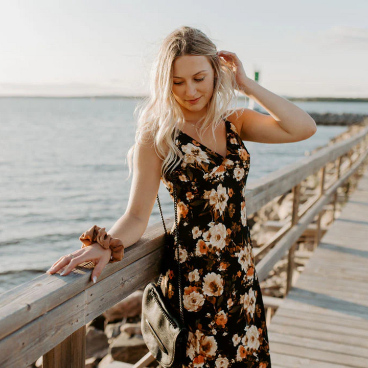 A rust-colored fabric scrunchie with a gathered, ruffled appearance. It has a small white tag with the word 