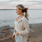 A rust-colored fabric scrunchie with a gathered, ruffled appearance. It has a small white tag with the word 