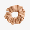 A rust-colored fabric scrunchie with a gathered, ruffled appearance. It has a small white tag with the word 