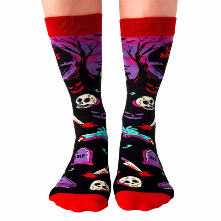 A pair of black socks with a Halloween-themed design. The socks feature a zombie hand, skulls, tombstones, and the phrase 