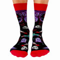 A pair of crew socks with a Halloween theme. The socks are mostly black with red and purple accents. The design includes a zombie hand, a graveyard with tombstones, a skull, and bats. The text "Scary Movies and Chill" is printed on the socks.