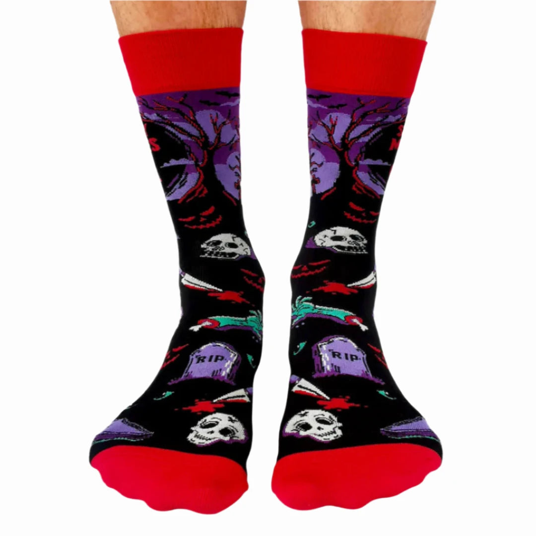 A pair of crew socks with a Halloween theme. The socks are mostly black with red and purple accents. The design includes a zombie hand, a graveyard with tombstones, a skull, and bats. The text "Scary Movies and Chill" is printed on the socks.
