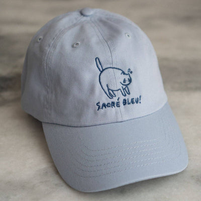 Gray cap with cat illustration and 'Sacère bleu!' text on a neutral background