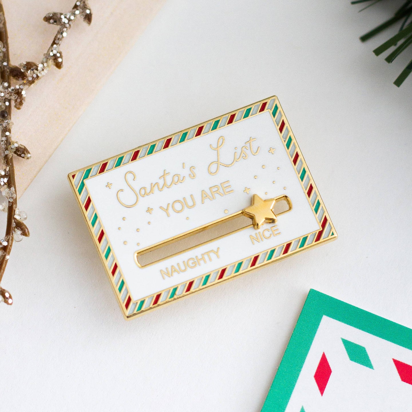 A gold-colored pin shaped like a Christmas list. The list has a slider that can be moved between "NAUGHTY" and "NICE." A star is placed on the slider.