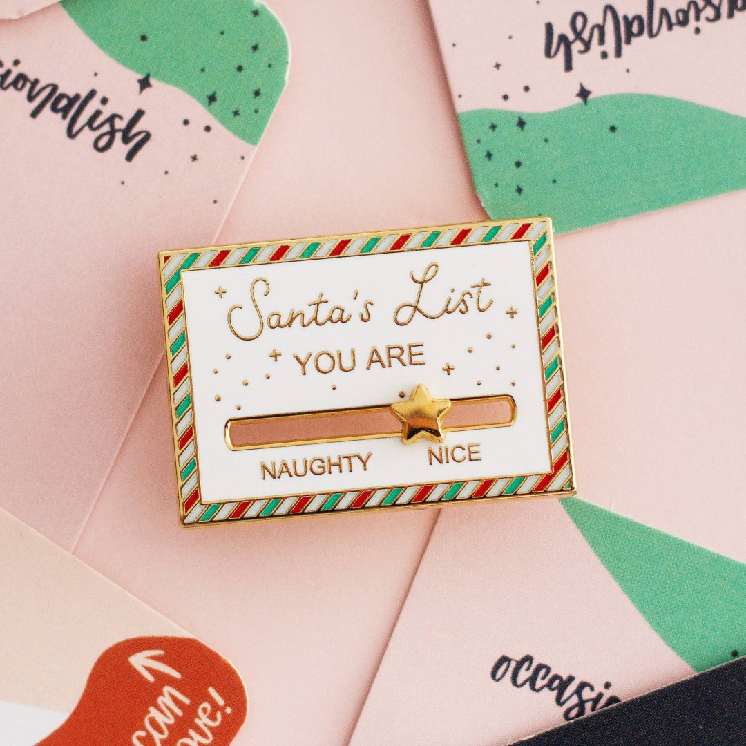 A gold-colored pin shaped like a Christmas list. The list has a slider that can be moved between "NAUGHTY" and "NICE." A star is placed on the slider.