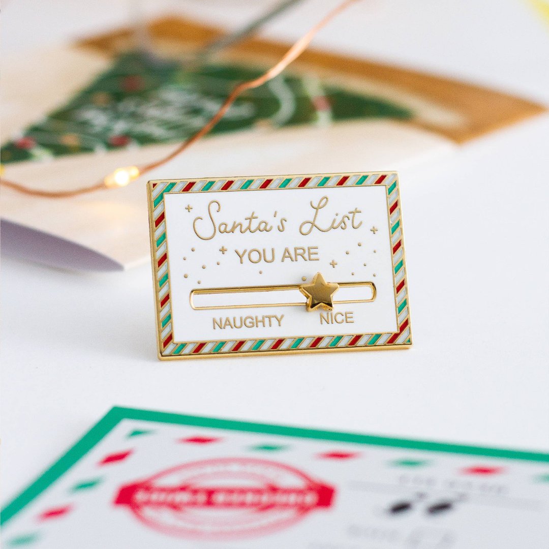 A gold-colored pin shaped like a Christmas list. The list has a slider that can be moved between "NAUGHTY" and "NICE." A star is placed on the slider.