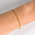 Gold bracelet on a wrist with a plain background
