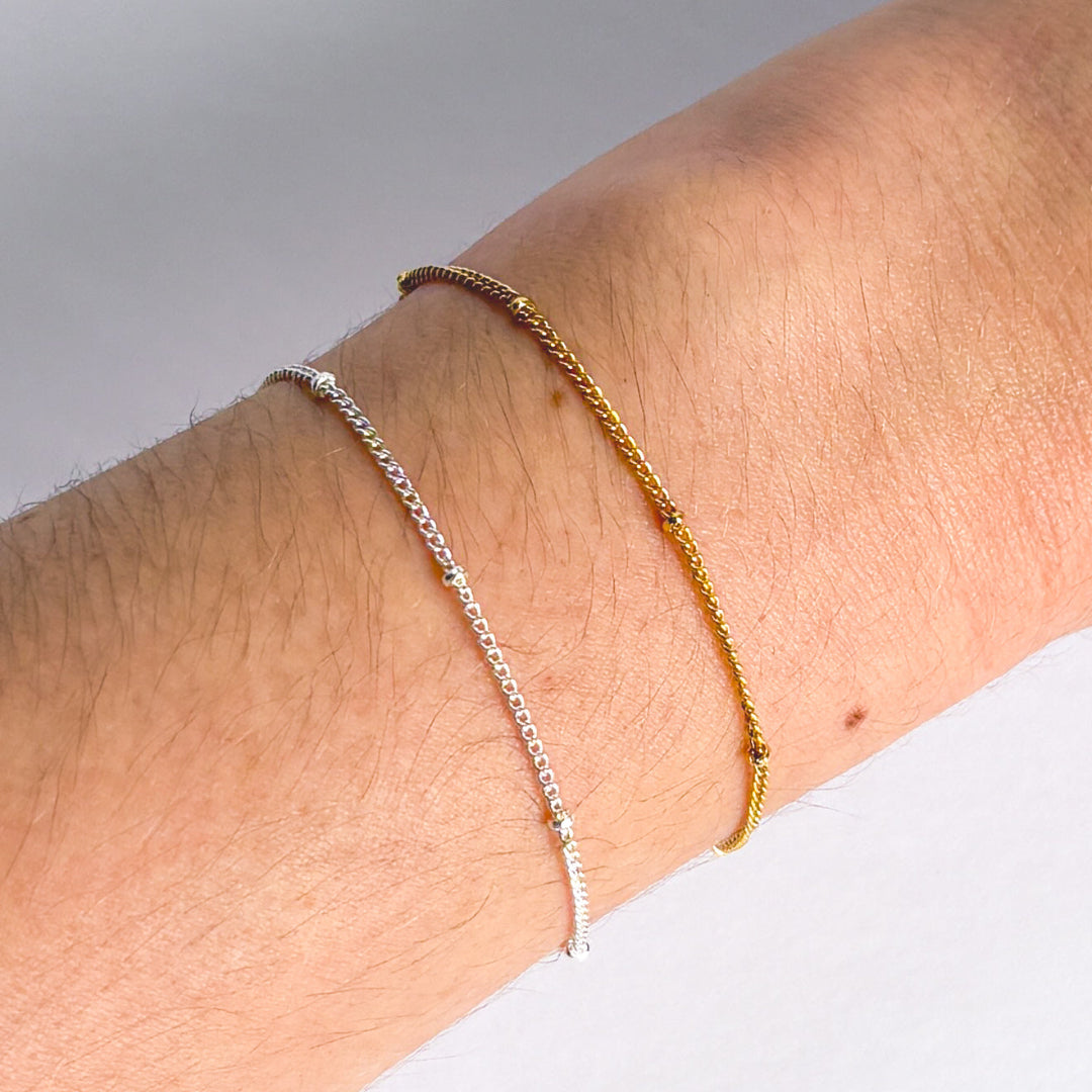 Two gold and silver bracelets on a wrist against a gray background
