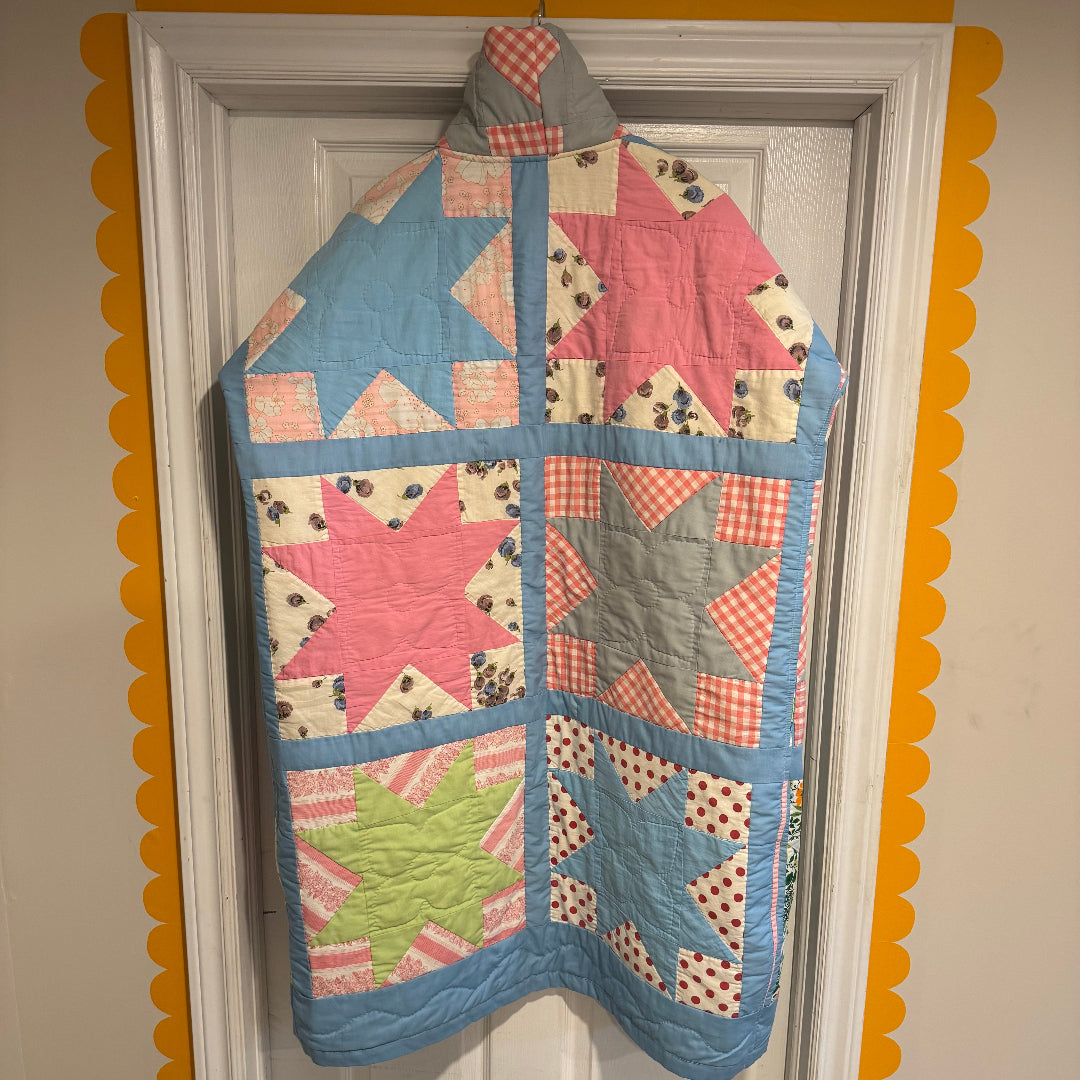 A long patchwork jacket made from pastel Sawtooth Star quilt blocks with a high collar and metal snaps, hanging on a white door framed by a yellow scalloped border.

If you’d like a more whimsical, minimalist, or fashion‑forward tone, I can shape the description however you like.