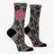 A pair of women's crew socks with a grey background and a pattern of black and white flowers on branches. One sock has text in bright pink that reads 