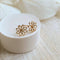 A pair of gold daisy stud earrings on a white background. The earrings have a delicate, openwork design with a small circle in the center of each flower.