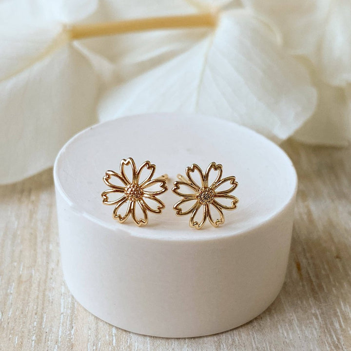 A pair of gold daisy stud earrings on a white background. The earrings have a delicate, openwork design with a small circle in the center of each flower.