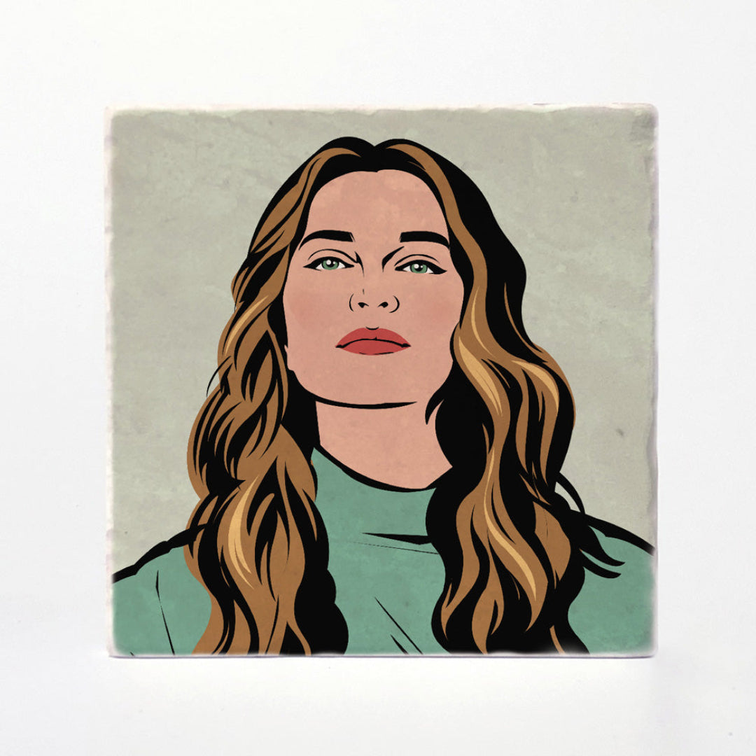 A square printed tile or coaster featuring a stylized illustrated portrait of a woman with long wavy brown hair, green eyes, red lips, and a mint green top on a pale gray background, shown against a white backdrop.