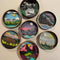 Eight circular, layered wooden shadow boxes depicting different nature scenes. The scenes include mountains, lakes, rivers, trees, a sunset, a starry night sky, a moon, and a bear. The boxes are painted in various colors and are arranged in a grid pattern on a gray surface.