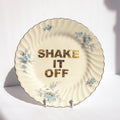 Decorative plate with floral designs and 'SHAKE IT OFF' text on a white background