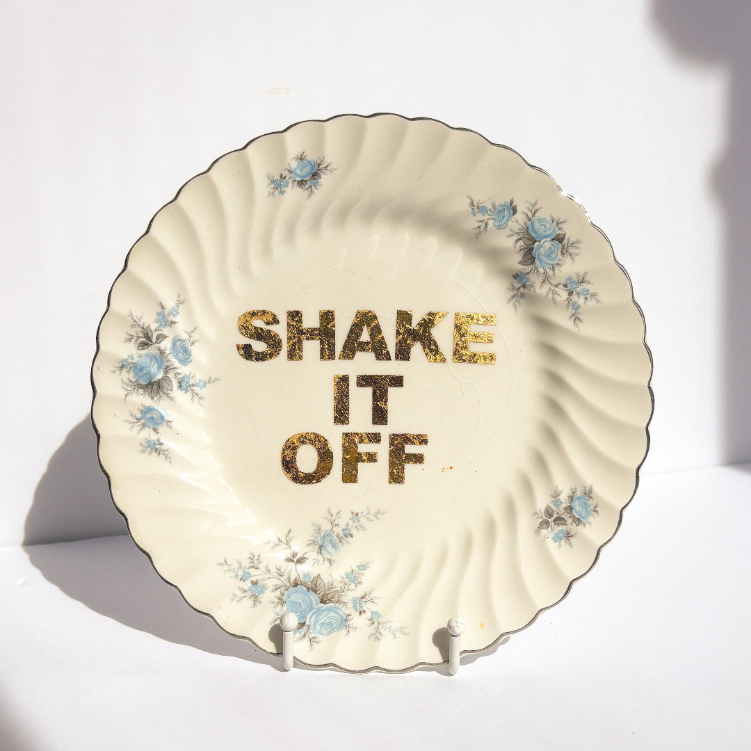 Decorative plate with floral designs and 'SHAKE IT OFF' text on a white background