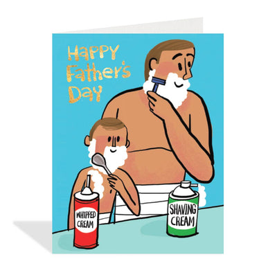 Light blue greeting card featuring a colourful cartoon illustration by Carlos Aponte of a light-skinned father with brown hair shaving his face with a razor, while a light-skinned child with brown hair stands next to him applying whipped cream to their face with a spoon. Two cans, one labeled 