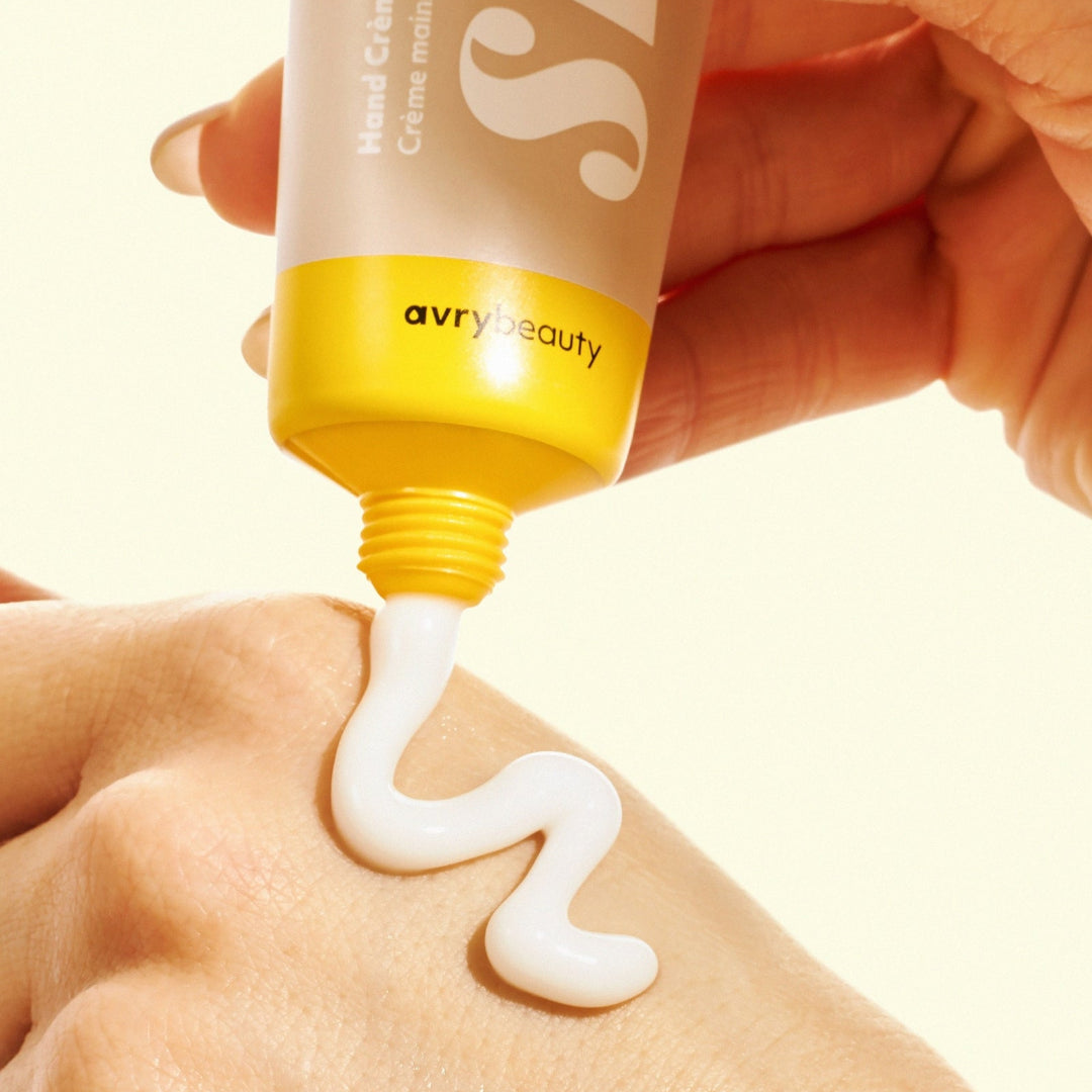 Hand applying cream from a 'avry beauty' tube onto skin