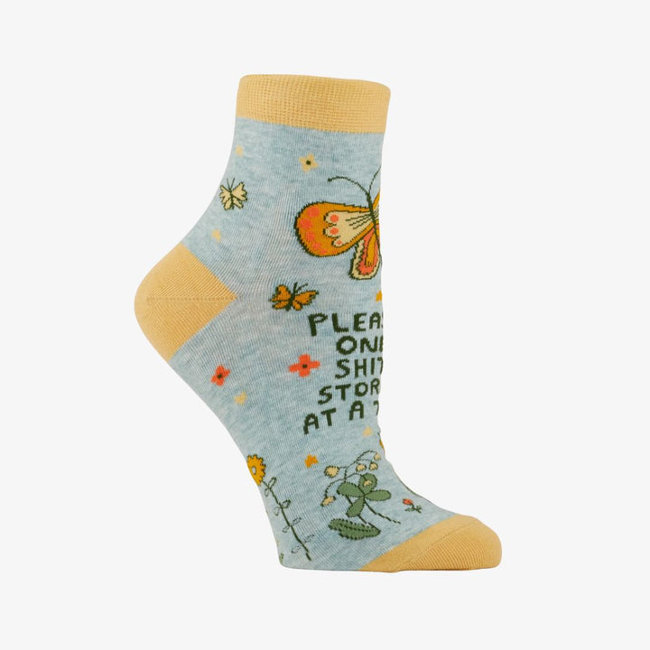 A pair of light blue ankle socks with yellow cuffs and toes. The socks feature an orange butterfly at the top and various small flowers and butterflies scattered across. Text on the socks reads 
