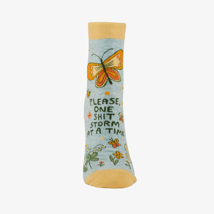 A pair of light blue ankle socks with yellow cuffs and toes. The socks feature an orange butterfly at the top and various small flowers and butterflies scattered across. Text on the socks reads 