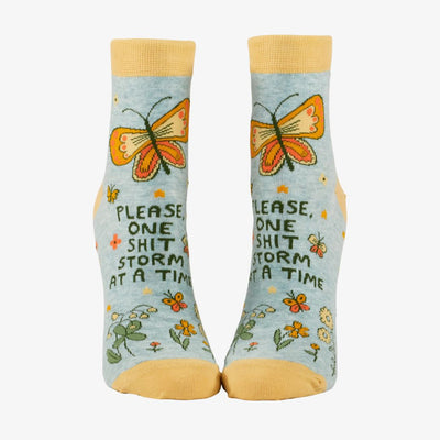 A pair of light blue ankle socks with yellow cuffs and toes. The socks feature an orange butterfly at the top and various small flowers and butterflies scattered across. Text on the socks reads 
