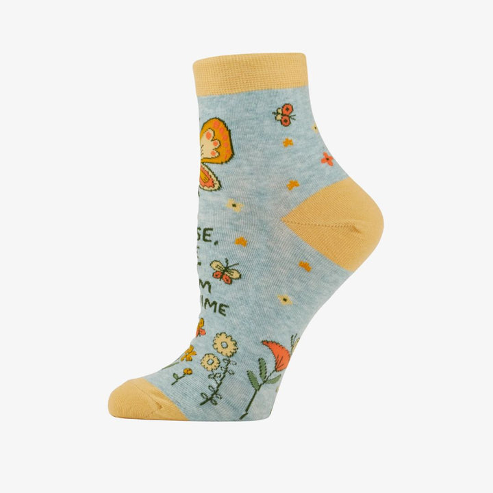 A pair of light blue ankle socks with yellow cuffs and toes. The socks feature an orange butterfly at the top and various small flowers and butterflies scattered across. Text on the socks reads 