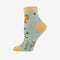 A pair of light blue ankle socks with yellow cuffs and toes. The socks feature an orange butterfly at the top and various small flowers and butterflies scattered across. Text on the socks reads 