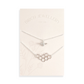 A pair of silver necklaces on a white card. The longer necklace features a honeycomb pendant, and the shorter necklace features a bee pendant. The card has the text "BIRCH JEWELLERY" and "EST-2011" printed on it.