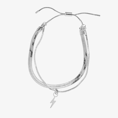 A set of two silver bracelets, one layered over the other, with a lightning bolt charm hanging from the bottom. The bracelets are displayed on a pink card with the brand name 