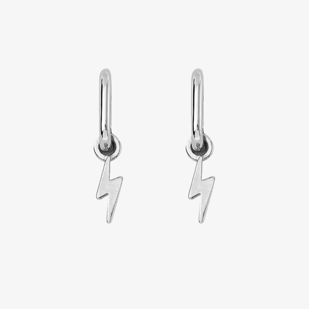 A pair of silver earrings with lightning bolt charms on a pink background. The earrings are displayed on a card with the brand name "Foxy Originals."
