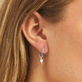 A pair of silver earrings with lightning bolt charms on a pink background. The earrings are displayed on a card with the brand name "Foxy Originals."
