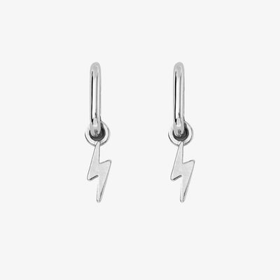 A pair of silver earrings with lightning bolt charms on a pink background. The earrings are displayed on a card with the brand name 