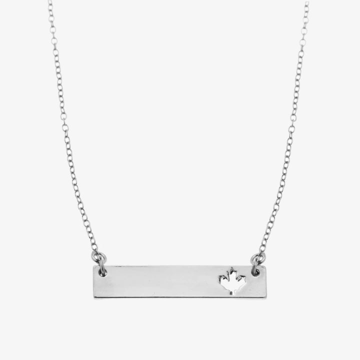 A silver necklace with a bar pendant. The bar has a cut-out maple leaf design.