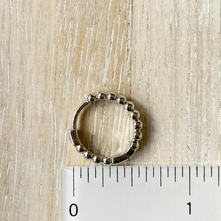 A pair of 925 sterling silver ball hoop earrings, featuring a beaded design, displayed on a white textured surface with white floral accents. The earrings are dainty and high-quality, available in Ottawa, Ontario, Canada.