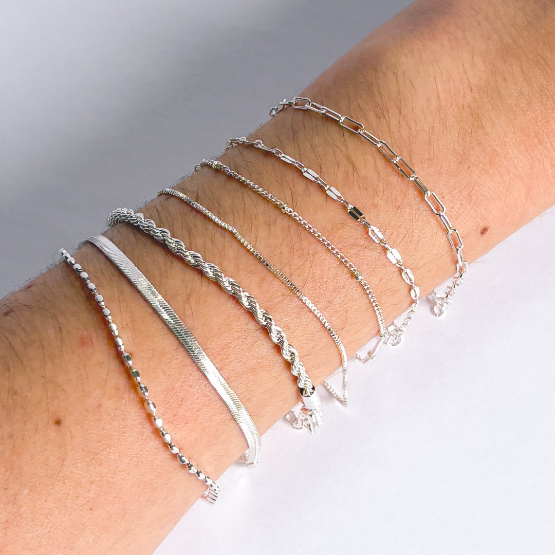 Silver bracelets on a wrist against a neutral background