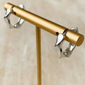 A pair of polished silver-toned hoop earrings displayed on a gold jewelry stand against a soft beige background.