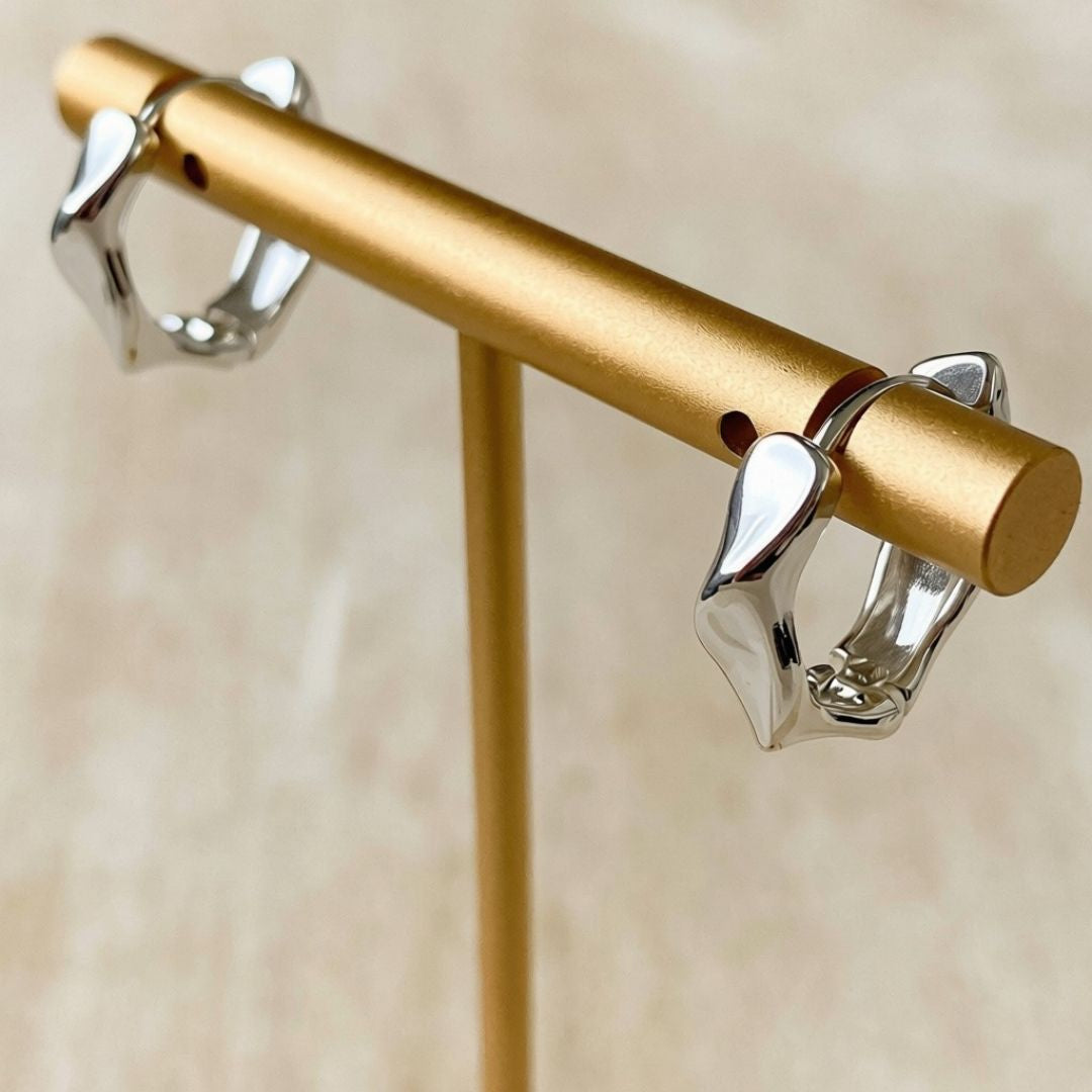 A pair of polished silver-toned hoop earrings displayed on a gold jewelry stand against a soft beige background.