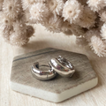 A pair of silver hoop earrings displayed on a marble-like surface with a bouquet of dried white flowers in the background.