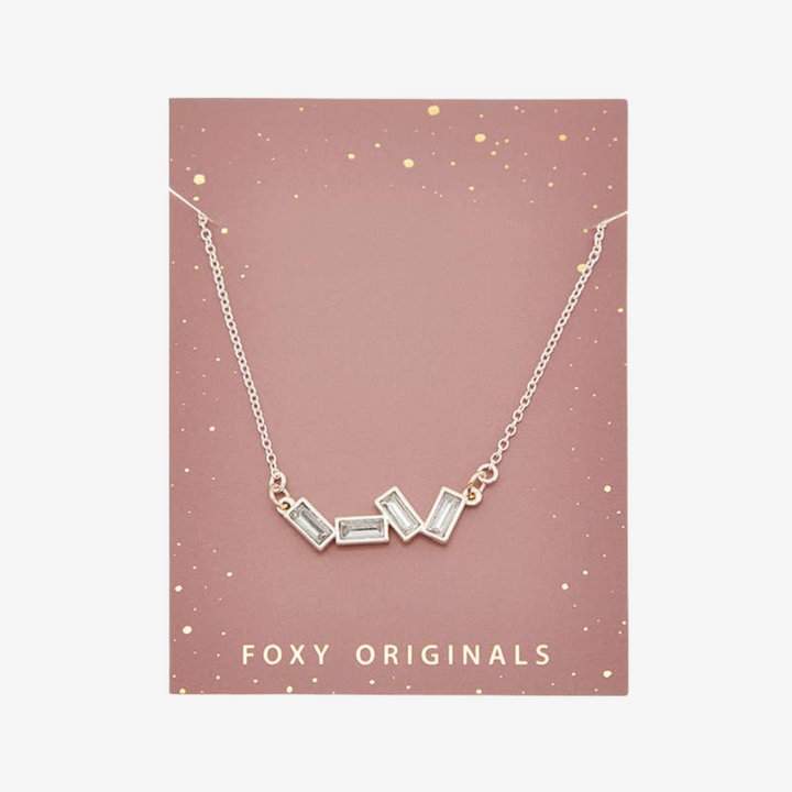 A silver necklace with several rectangular-shaped crystals on a pink card with the brand name 