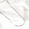 A silver herringbone chain necklace resting on a white surface. The chain is flat and has a wavy, snake-like pattern.