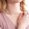 A silver herringbone chain necklace resting on a white surface. The chain is flat and has a wavy, snake-like pattern.