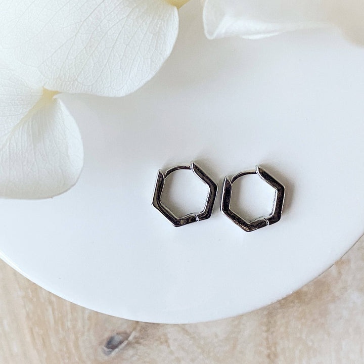 A pair of silver Hexi huggies, featuring a minimalist, hexagon hoop design, displayed on a white ceramic dish with white floral accents. The earrings are geometric and modern, available in Ottawa, Ontario, Canada.