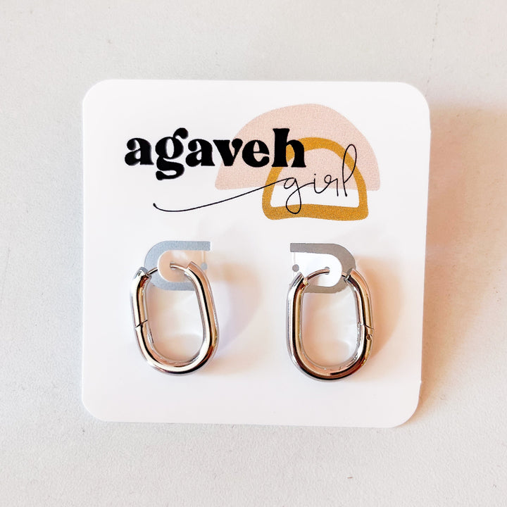 A pair of Agaveh Girl Silver Layla Hoops, featuring a chunky, rounded oval design, displayed on a branded card with the text 'agaveh girl,' against a textured background. The earrings are minimalist and modern, available in Ottawa, Ontario, Canada.